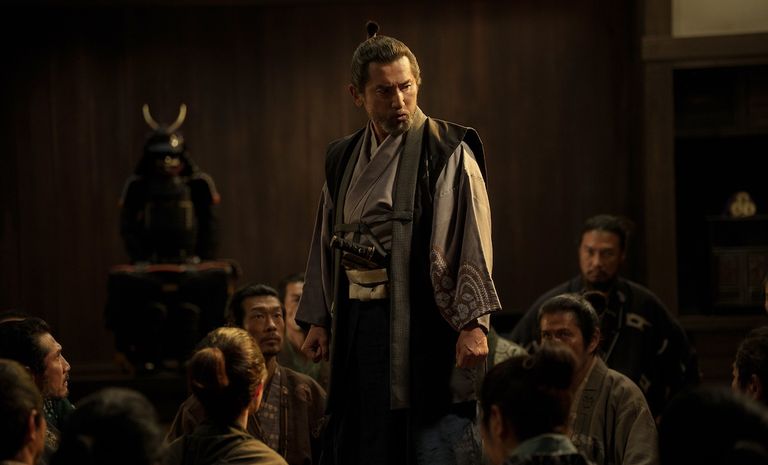The Samurai and the Prisoner theatrical production scene featuring a samurai standing amidst seated characters in historical Japanese attire.